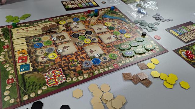 Castles of Burgundy is an old favourite. This new version is more colourful and the board is a little easier to parse. The background is a red-tiled roofs of a medieval city with light, tan plazas which help the greens and blues pop a bit better. Great game, one every gamer should play.