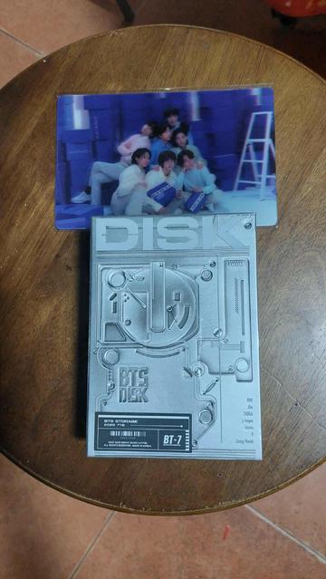 A silver box that says BTS Disk that contains the BTS 7 Moments materials. On top is a preorder benefit lenticular card of BTS.