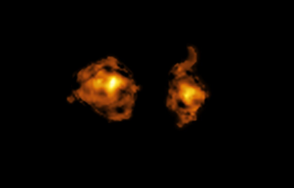 A telescopic image of two galaxies, shown as bright clouds of swirling gas against the pitch-dark backdrop of deep space. The galaxies are shown in bright yellows and oranges that get more intense at their centres and fade towards their edges.