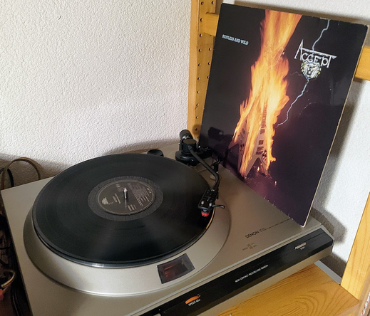 Accept's album "Restless and Wild" playing on a Denon DP-30L turntable. The cover shows two upright Gibson Flying-V guitars leaning against each other, while being on fire.