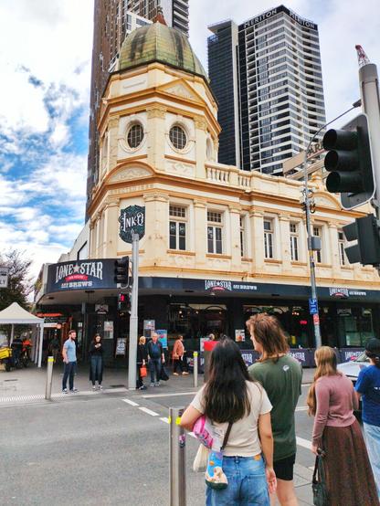 A three storey colonial building with a green copper dome on top, painted in three shades of cream. There is a Lone Star restaurant on the ground floor. It is photographed from across the street, with a crowd of people waiting to cross.