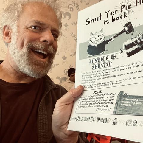 smiling man with white hair holds up comedic zine