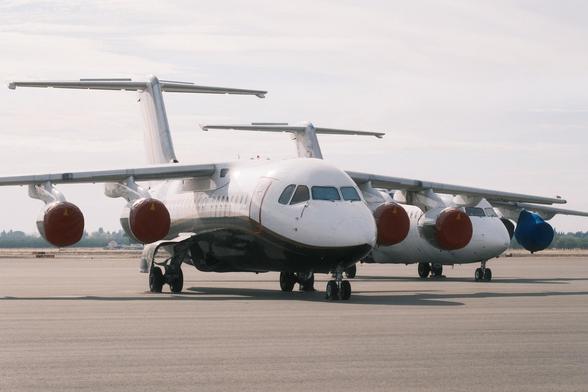 Two parked BAE-146 on a tarmac, noses facing the photographer obliquely, with protective orange covers over their engines.