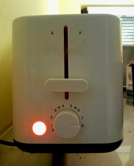 A toaster's power light glows as it toasts toast round side down.