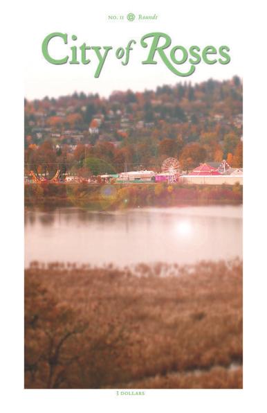 No. 11, “Rounds.” Away across a stretch of placid water a tiny amusement park is nestled in autumnal foliage, bright curls of super slide and roller coaster, the red roof of a skating rink, the towering round of a Ferris wheel, so delicate at this distance. Beyond a hill rises under the colorless sky, houses scattered along the face of it among a mix of turning deciduous trees, brown and red and umber, and fixedly greenly dark conifers.