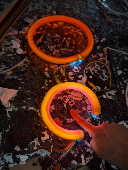Pink horseshoe on paint drip table with my finger (all pink) inside of it and gold light going around it. A brown circle behind it.