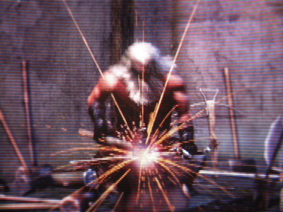 Sparks fly as Andre of Astora hammers a weapon on his anvil.