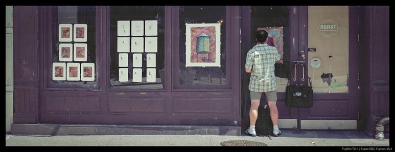 A person hangs up numerous pieces of art on the glass windows of a closed-down store, its doors bolted and partially papered over.