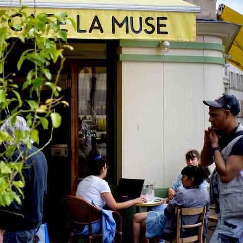 People at the Cafe La Muse, with one person working on a laptop at a table outside.