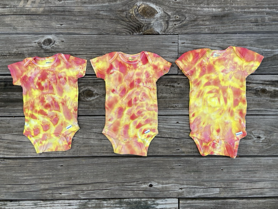 Three sizes of baby bodysuits, hand dyed in shades of orange, peach and yellow