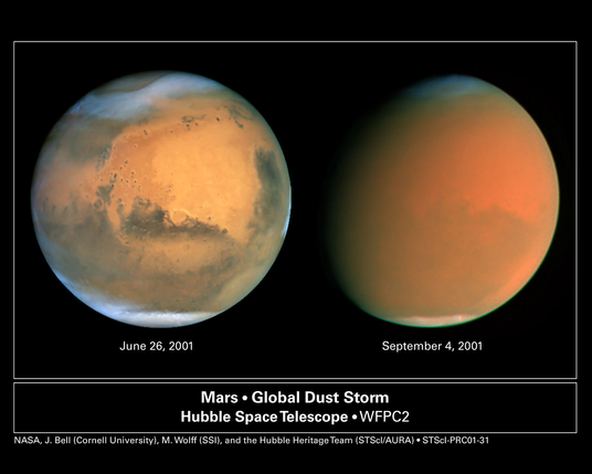 Side-by-side images of Mars taken by the Hubble Space Telescope during a dust storm in 2001. The left image, dated June 26, 2001, shows a clear view of the Martian surface with visible dark regions, craters, and polar ice caps. The right image, dated September 4, 2001, shows Mars obscured by a thick orange haze caused by the dust storm, with most surface features hidden. Below the images is a label that reads "Mars • Global Dust Storm – Hubble Space Telescope • WFPC2" and credits to NASA, J. Bell (Cornell University), M. Wolff (SSI), and the Hubble Heritage Team.