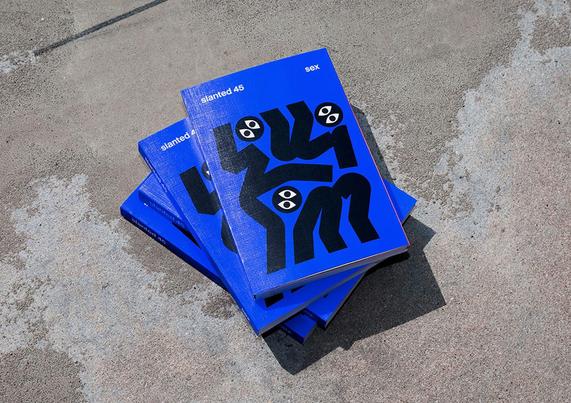 Three copies of "Slanted 45" stacked on a textured surface, featuring bold blue covers with black abstract art and playful eyes.