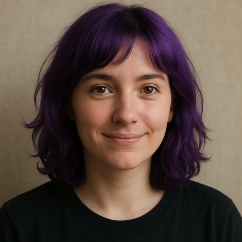 A close-up portrait of a young woman with short, wavy, dark purple hair.  She's wearing a dark-colored t-shirt and has a pleasant, slightly smiling expression.  The background is a neutral beige.