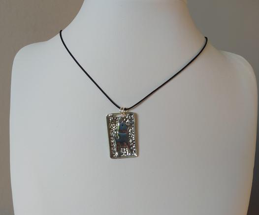 a square silver pendant with a black cord. it has the profile of a dog on it made also from silver.