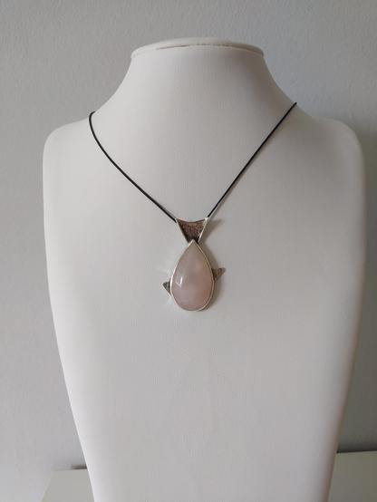 a silver fish shaped pendant with black cord. it has a big pink teardrop shaped gemstone
