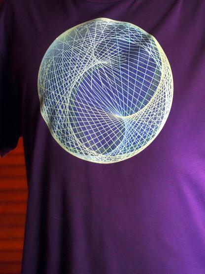 Photograph of the front of a purple T-shirt depicting blue-green geodesics on an ellipsoid with unequal axes, looking like an elliptical string diagram.