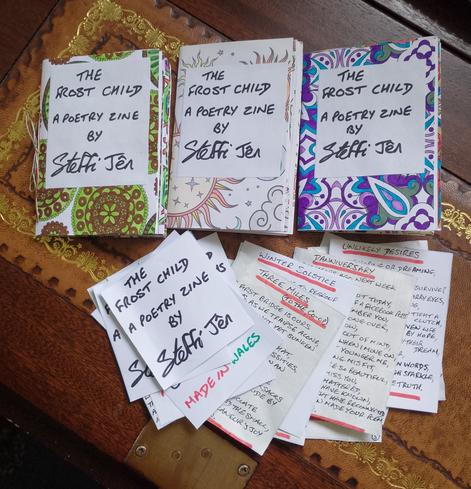 Three mini poetry zines on the wooden desk flap of an old bureau. Each zine looks different because they're made from colouring book pages with bright abstract designs.
There's also a pile of hand written titles and poems waiting to be glued into more books when I have made them.