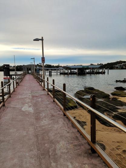 Looking down the well-worn pier to the ferry stop. A patch of blue sky is visible through the clouds.