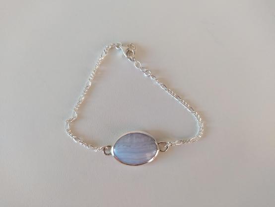 a silver bracelet placed in white background. it has a light blue oval gemstone