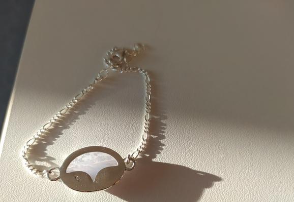 the back side of a silver bracelet placed in white background. it's under intense side lighting and we can see the semi transparent light blue gemstone