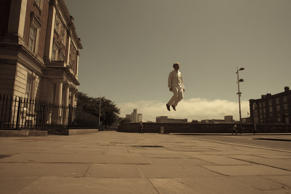 Person floating in mid-air on a paved urban sidewalk beside a large building.