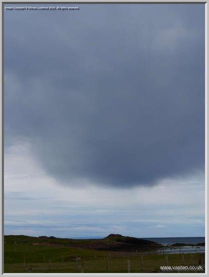 A dark grey cloud points down exactly over the pimple in the landscape that is the remains of Clachtoll Broch