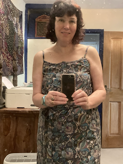 Middle aged woman in cotton dress with spaghetti straps, button front and tie belt in purple print