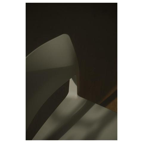 Photo der Lehne eines grauen Vitra Kunststoff Stuhls. Der Hintergrund verschwindet im tiefen Schatten. Diffuse Farben und mattes Licht prägen das Bild.