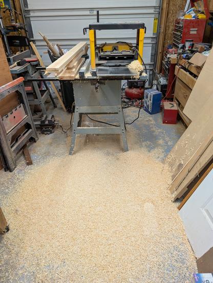 A planer on top of a table saw with a huge pile of planer shavings on the floor.