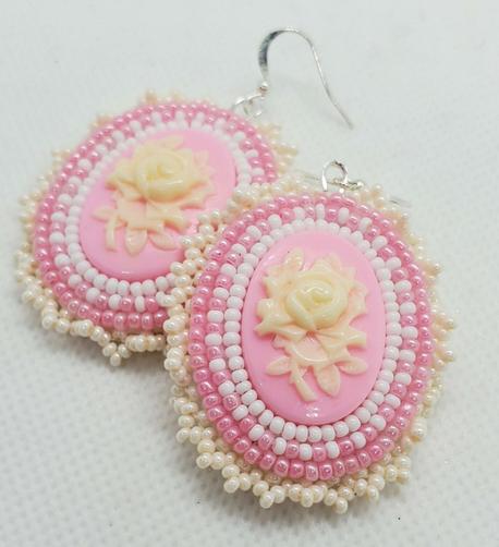 an elegant pair of beaded earrings made by kiamichi. the centerpiece is a cream colored rose on a light pink background surrounded by clear, pastel pink, and pearlescent beads to accentuate.