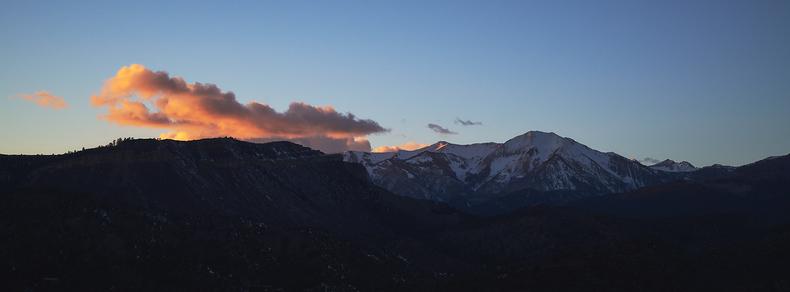 Snow-capped mountains at sunset with a glowing orange cloud above and a clear blue sky.