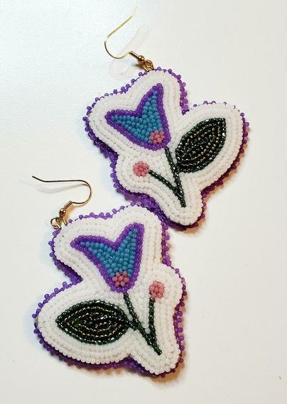 a pair of beaded earrings by kiamichi of crocus shaped flowers in blue and purple with a big green leaf bordered by white