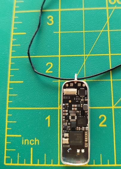 a silver pendant with an old PCB. it has a black cord and it's placed on green mat