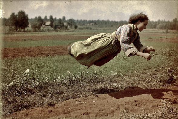 Person floating horizontally above a rural landscape in vintage attire.