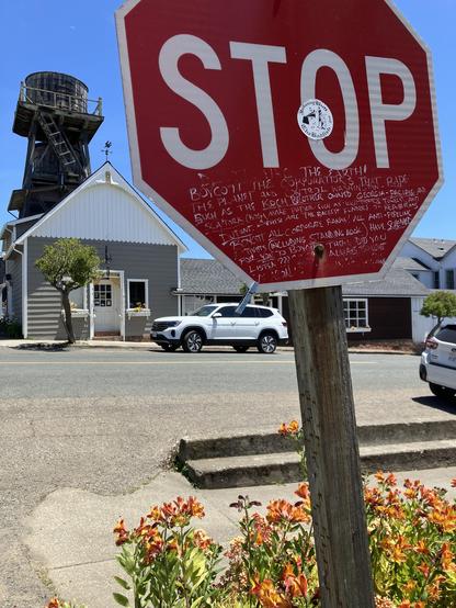 In Mendocino, a stop sign has white graffiti under the word that leads off by saying STOP destroying the earth! It’s hard to read, but it continues with warnings about the Koch Brothers owning Georgia Pacific lumber and the need to boycott corporate banks.

In the background are typical Mendocino Victorian buildings and a wooden water tower. At the base of the sign are a bunch of blooming Peruvian lilies.