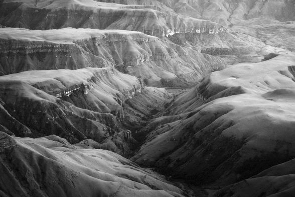 A massive valley resembling the Grand canyon seen in monochrome with high contrast from the recently risen sun.
