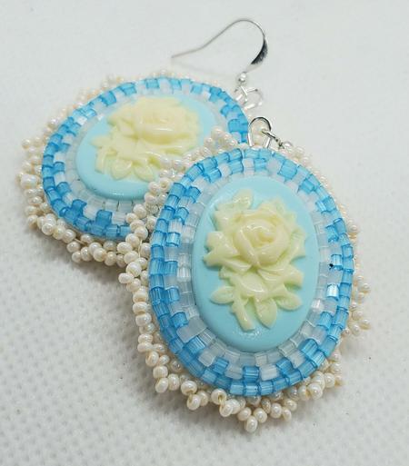 a pair of elegant beaded earrings. the centerpiece is a cream colored rose on a light blue background. the surrounding beads are pale blue and clear and pearlescent to accentuate