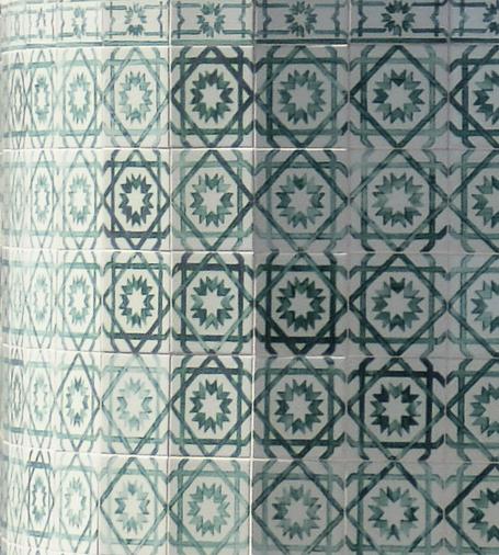 Green and white tiles on a curved wall. Each square tile has a central white twelve-pointed star surrounded by green chevrons. Green overlapping squares make eight-pointed stars with a quarter of an eight-pointed star at the corners.