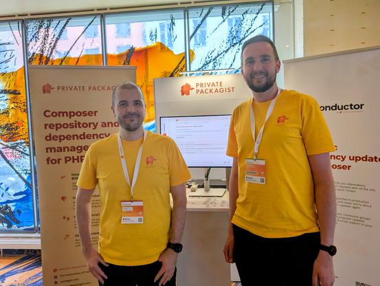 Igor Benko and Nils Adermann in yellow Private Packagist t-shirts in front of a Private Packagist expo booth.