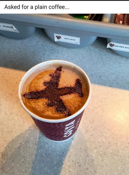 Photo of a cup of coffee with light brown foam at the top. The foam has been moved so that there is an airplane drawn on the coffee. Meme caption reads, "I asked for a plain coffee."