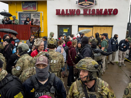 Law enforcement officers wearing protective gear with FBI, ATF and Homeland Security Investigations insignia stand on Bloomington Avenue near Lake Street in south Minneapolis as protesters respond to a law enforcement action on Tuesday.