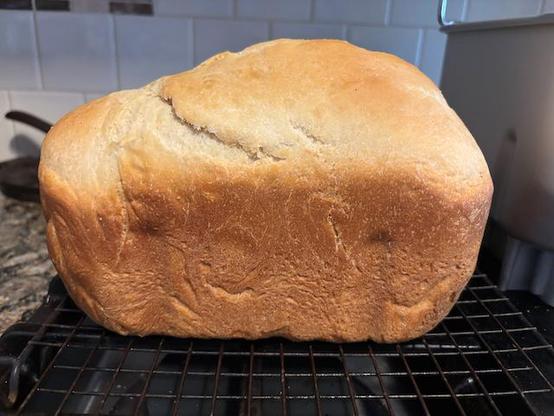 A loaf of bread fresh out of the bread machine. It looks like a traditional rectangular loaf but one side is noticeably bulging up giving it an uneven appearance.