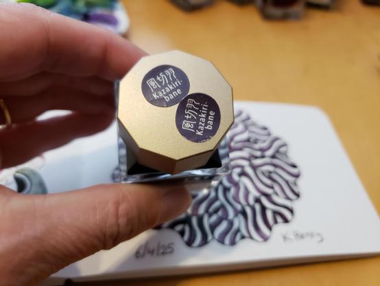 I'm holding a bottle of ink with Japanese text on it. Behind the bottle is my drawing for the day in my sketchbook. The abstract pattern is floral.