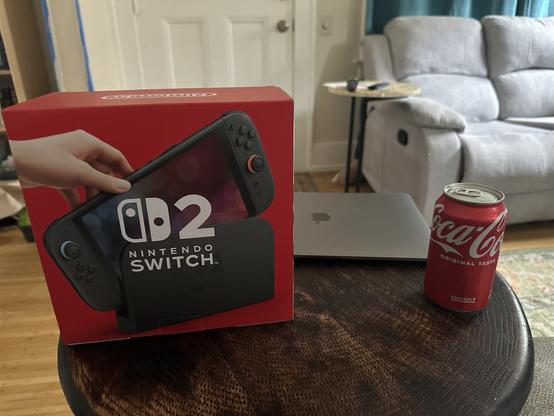 Image of a Nintendo Switch 2 console in its box sitting on a side table next to a laptop and a can of Coca-Cola.