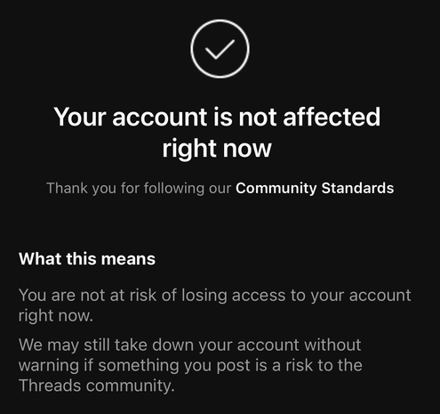 The image features a black background with white and gray text. At the top, there is a white circle with a downward-pointing checkmark inside it. Below the icon, the text reads "Your account is not affected right now" in large white letters. Beneath this, in smaller gray text, it says "Thank you for following our Community Standards." Further down, the text "What this means" is displayed in white, followed by two bullet points in gray. The first bullet point states, "You are not at risk of losing access to your account right now." The second bullet point reads, "We may still take down your account without warning if something you post is a risk to the Threads community." The overall design is simple and clear, with a focus on conveying important information about account safety and community standards.