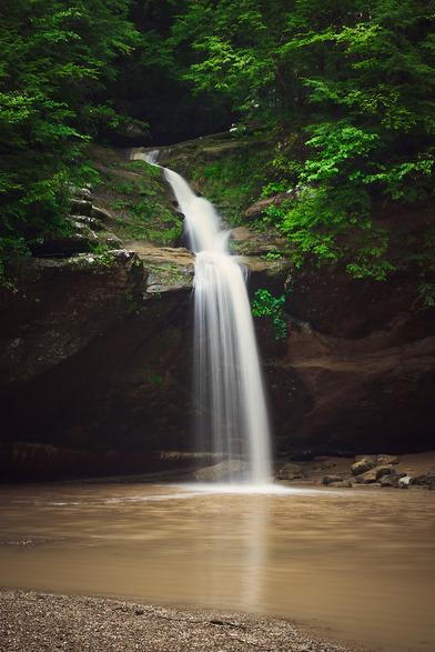 A waterfall cascading over rocks into a tranquil pool, surrounded by lush green foliage.