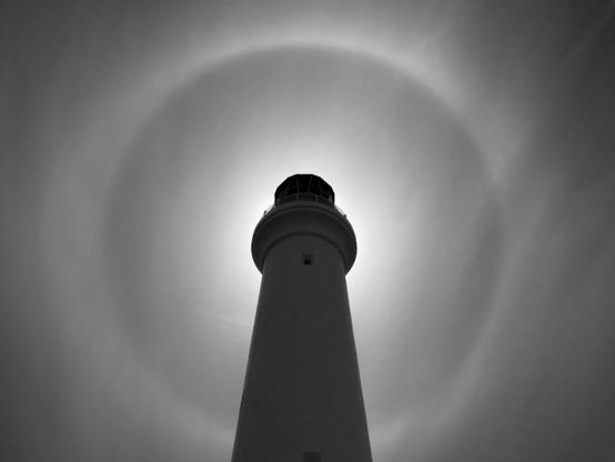 Lighthouse Effect - black and white is a photograph taken in Australia. The sun is behind the lighthouse and the astonished ring of light was visible in the sky.