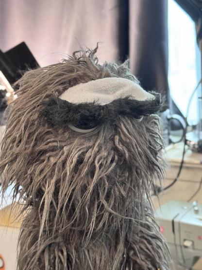 Grey furry live hands monster puppet with large glossy eyes, closeup view with eyes half closed