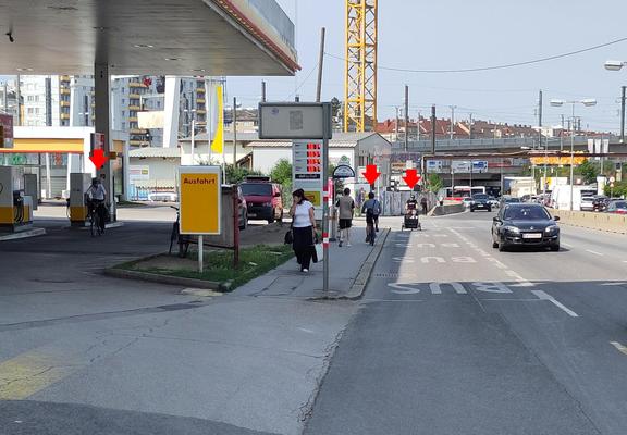 Foto der zweispurigen Richtungsfahrbahn plus Busspur, eine Person radelt auf der Buspur, eine am Gehsteig (gegen die Richtung), eine Person radelt durch die Tankstelle.