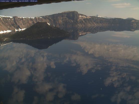 View of Crater Lake National Park from the Sinnott Memorial Overlook today. Clouds are reflected in the lake. A hint of snow remains in some of the less exposed areas around the lake. Park visitors can access some lake overlooks but most of Rim Drive, as well as the park’s north entrance, remain closed.